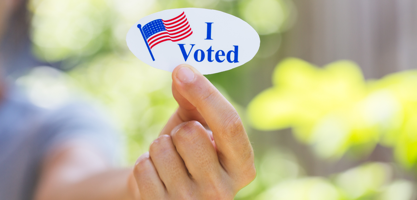 A close up photo of a someone's fingers holding an "I Voted" sticker.