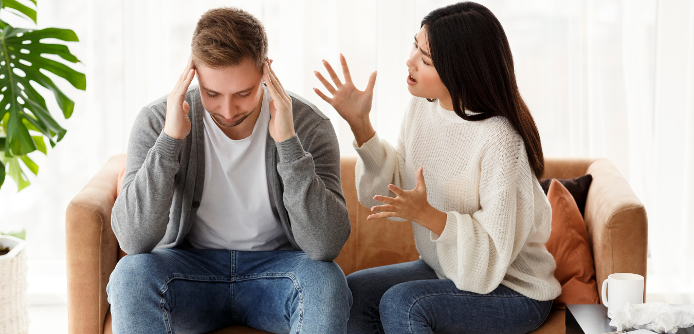 A man and a woman sitting on a sofa arguing.